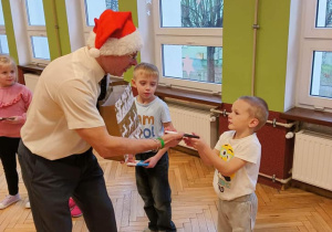 dorosły w czapce mikołaja rozdający upominek dzieciom