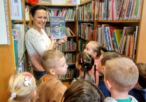 sala bilioteczna, regały z książkami, dzieci, kobieta z książką w ręku