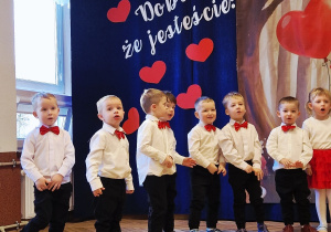 grupka przedszkolaków, eleganckie stroje, w tle baner dekoracyjny