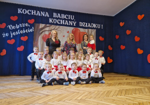 grupka przedszkolaków, eleganckie stroje, nauczycielki, w tle baner dekoracyjny