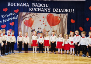 grupka przedszkolaków, eleganckie stroje, w tle baner dekoracyjny