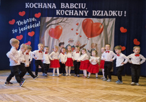 grupka przedszkolaków, eleganckie stroje, w tle baner dekoracyjny