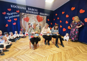 grupka przedszkolaków, na krzesłach babcie obierające jabłka