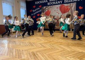 przedszkolaki tańczące w parach, w tle baner z napisem
