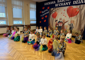 kucające przedszkolaki z kolorowymi chustkami w rękach, w tle baner