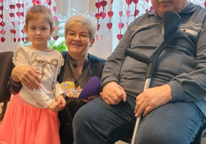 dziewczynka z babcią i dziadkiem, w tle dekoracja na oknie