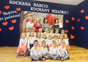 grupa przedszkolaków, nauczycielki, w tle dekoracja z napisem