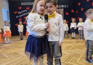 dziewczynka chłopiec z mikrofonem, w tle przedszkolaki