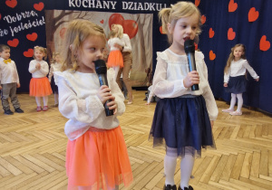 dziewczynki z mikrofonami, w tle przedszkolaki, baner dekoracyjny