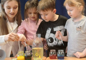 przedszkolaki, uczennica w białym fartuchu, płyny w szklanych pojemnikach