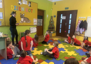 sala przedszkolna, przedszkolaki w czerwonych koszulkach, nauczycielka w przebraniu kota