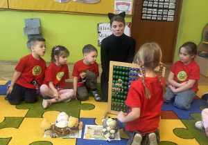 sala przedszkolna, przedszkolaki w czerwonych koszulkach, maskotki, liczydło