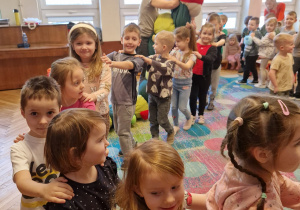 sala gimnastyczna, przedszkolaki ustawione w "pociąg", maskotka-gąsienica