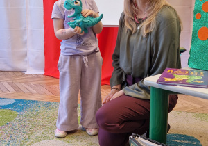 dziewczynka w opasce na oczach, zabawka dinozaur, pani, książki