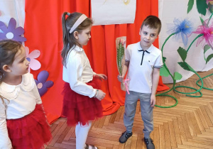 2 dziewczynki, chłopiec z kwiatkiem w ręku