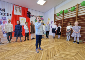 grupa przedszkolaków, chłopiec z mikrofonem, dekoracja z okazji 8 marca