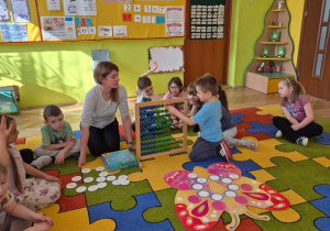 sala przedszkolna, przedszkolaki, nauczycielka, liczydło, duży kolorowy motyl na dywanie