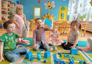 przedszkolaki z rękawicami na rękach, niebieskie klocki na dywanie