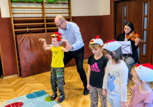 sala przedszkolna, skrzypaczka, mężczyzna czworo przedszkolaków w czapeczkach "kurki"