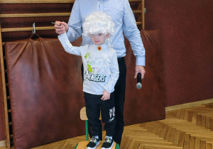 sala przedszkolna, mężczyzna, przedszkolak w białek peruce stojący na krześle