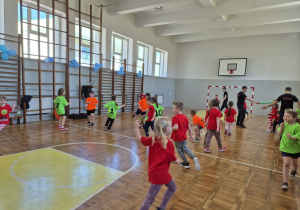szkolna sala gimnastyczna, biegające przedszkolaki, dwóch nauczycieli