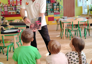 sala przedszkolna, osoba dorosła z obrazkiem grzybów, przedszkolaki