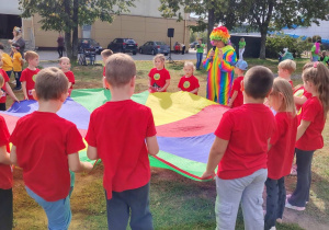 przedszkolaki w czerwonych koszulkach trzymające chustę animacyjną, osoba w przebraniu klauna