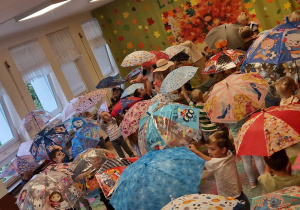 sala przedszkolna, duża grupa tańczących przedszkolaków z rozłożonymi parasolami