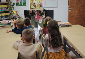 sala biblioteczna, przedszkolaki, pani bibliotekarka z obrazkiem w ręku