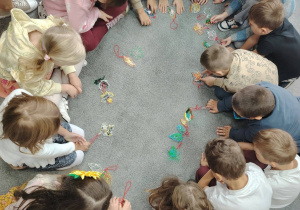 grupa przedszkolaków siedzących w kręgu, w środku wykonane przez nich listki metodą 3D