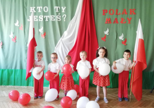 dzieci ubrane uroczyście , stojące na tle polskich symboli