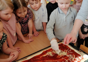 grupka dzieci i chłopiec sypiący ser na pizzę