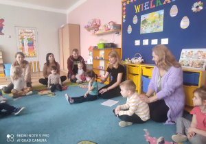 dzieci i doróśli siedzący na dywanie w sali przedszkolnej