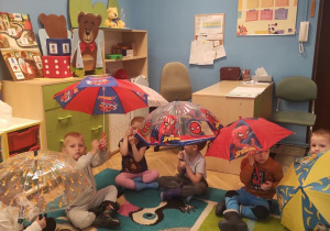 siedzące na dywanie dzieci z parasolkami