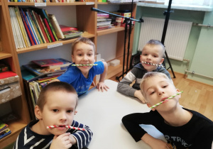 czterech chłopców ze słomkami w zębach siedzący przy stoliku